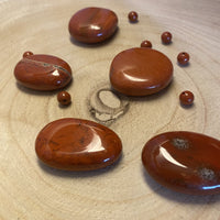 Spécimens de jaspe rouge sous forme de galets polis et petites pierres roulées, présentant des nuances allant du rouge brique au rouge profond